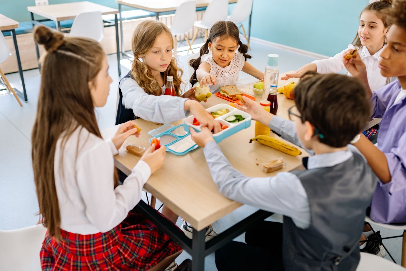 Primary school children eating lunch together at a table in a school dining hall